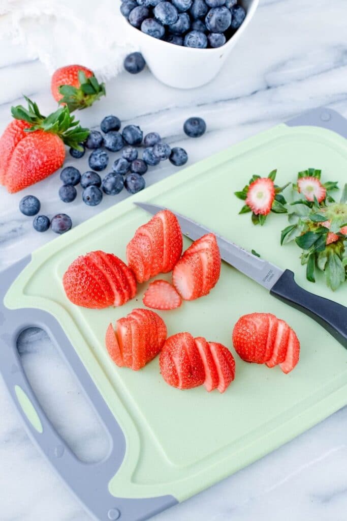 sliced berries on a cutting board and blueberries to side of cutting board on counter