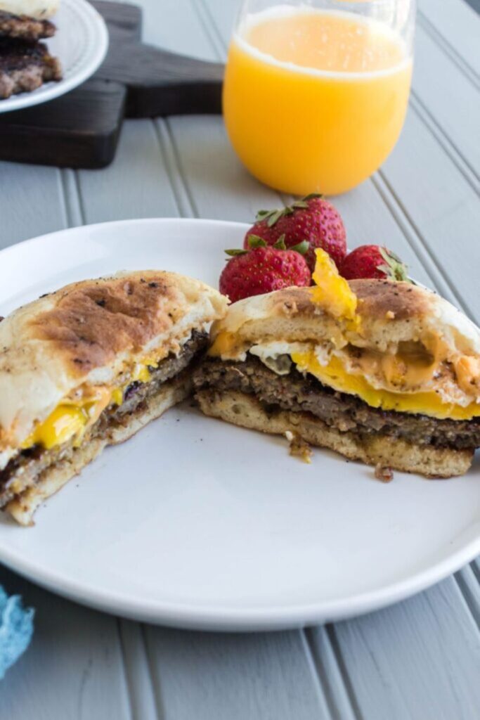 sausage egg and cheese mcmuffin cut in half on plate with orange juice behind it on table