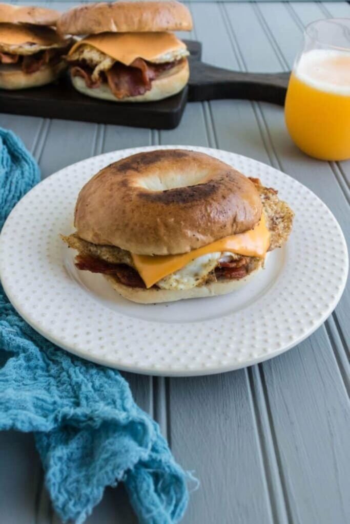 breakfast sandwich on a plate with orange juice in a glass behind it