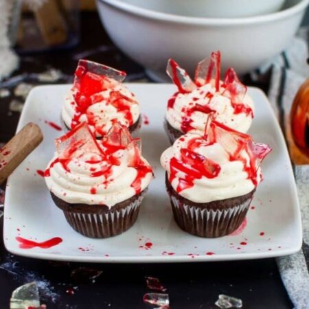 Bloody Cupcakes on a white plate on table with bowls and more fake glass sprinkled around table