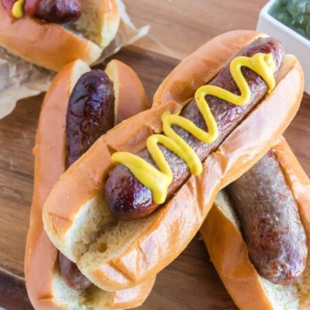 bratwurst in buns on table with the top brat drizzled with mustard