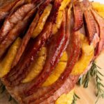 Brown Sugar Pineapple Ham on a wooden cutting board with fresh herbs around it
