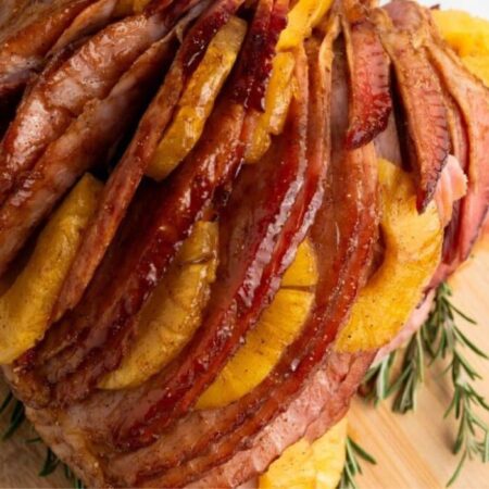 Brown Sugar Pineapple Ham on a wooden cutting board with fresh herbs around it