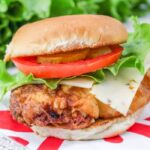 spicy chicken sandwich on table with lettuce, tomatoes, and cheese