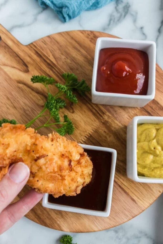 chicken strip being dipped in bbq sauce on table