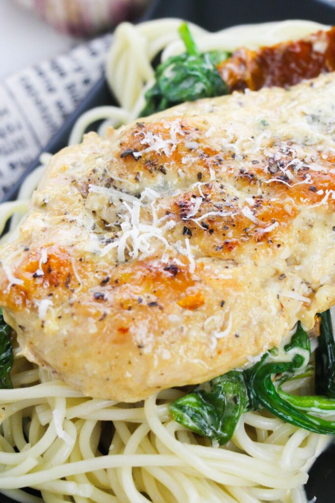 Tuscan chicken on top of a bed of pasta on a plate sitting on a table
