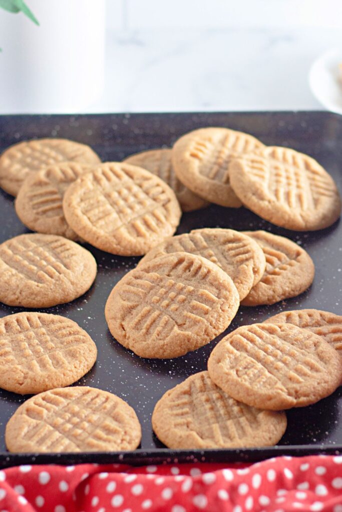 peanut butter cookies on a baking sheet scattered on tray with a red polka dot towel in the front of the pan