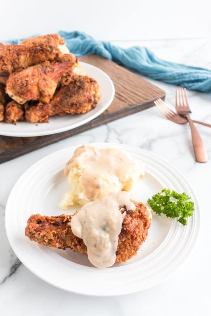 Fried Chicken Legs piled on a plate with a chicken leg with gravy over the top on plate with mashed potatoes