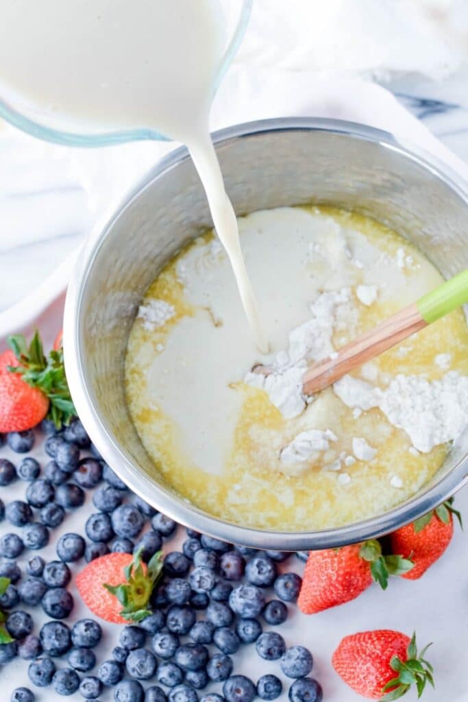 mixing pancake batter in a bowl with milk pouring into the metal bowl