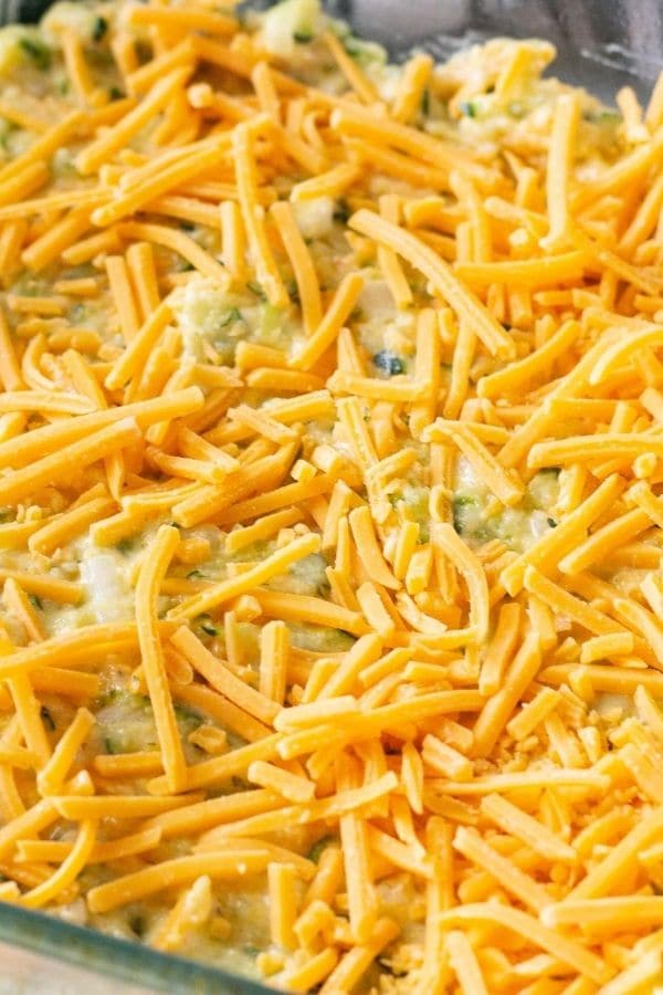 raw zucchini cornbread in a casserole with shredded cheese on top