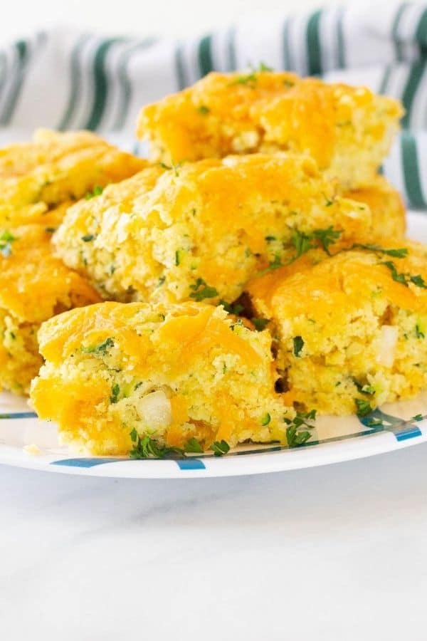 zucchini cornbread cut into squares and placed on a plate all stacked up
