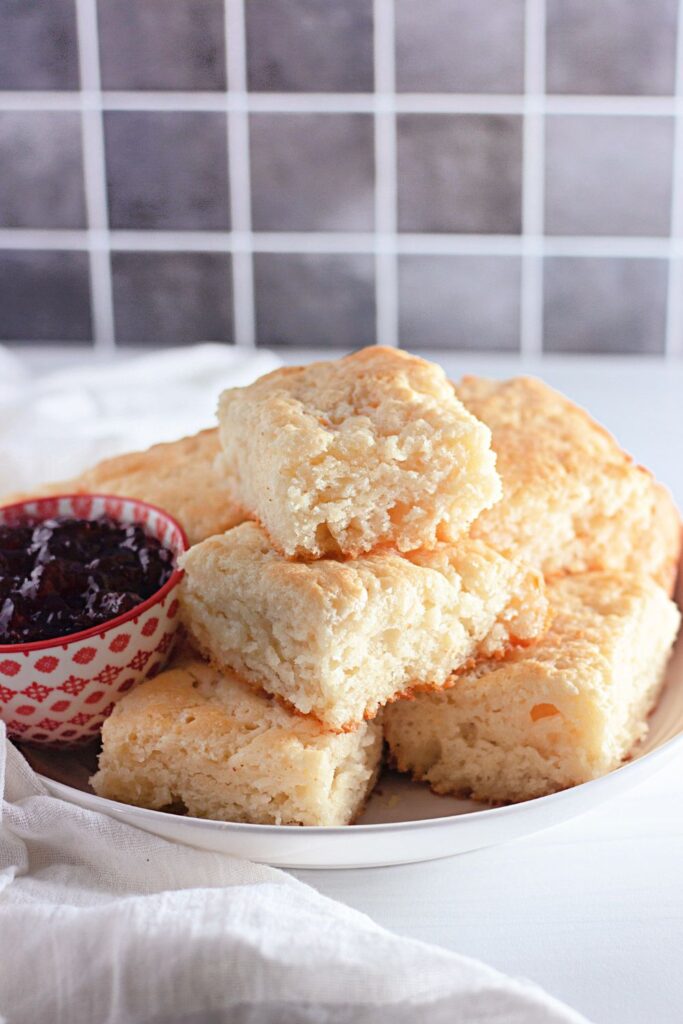 butter biscuits stacked on plate on table with grape jelly around it