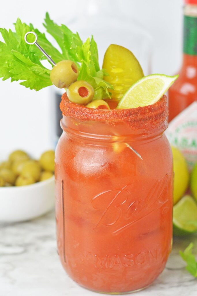 view of a bloody maria in a mason jar garnished with olives and lime wedges