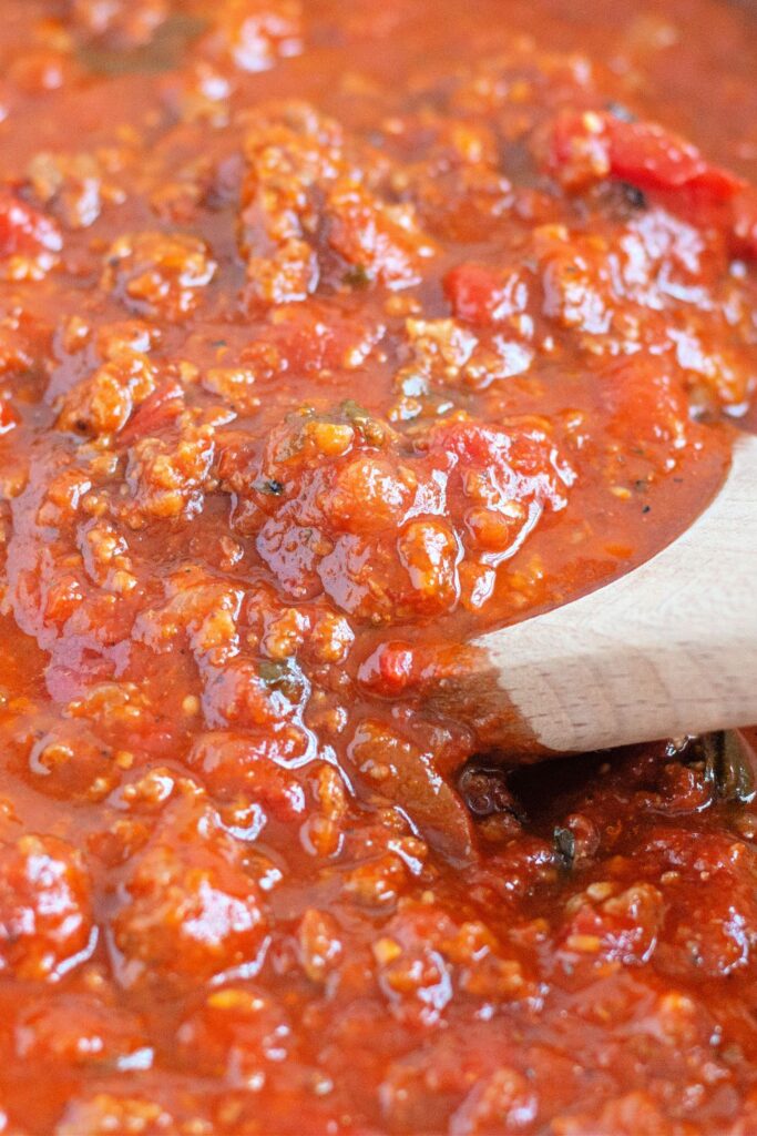 close up of meat sauce in a pot with a wooden spoon in pan