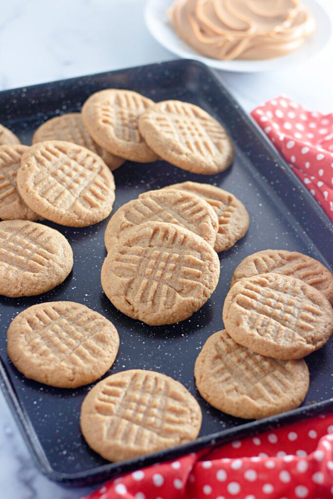 peanut butter cookies on a baking tray stacked on top of each other and scattered on pan