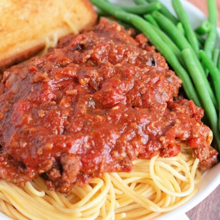 side view of spaghetti with sauce, garlic bread and green beans on a white plate