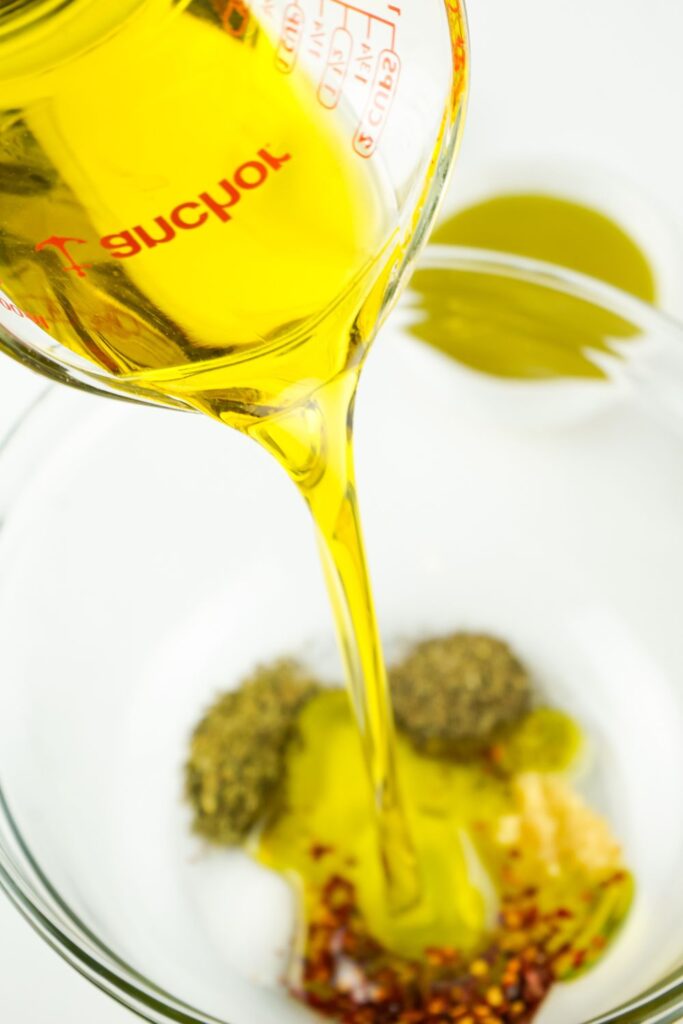 pouring oil into a bowl with herbs and spices