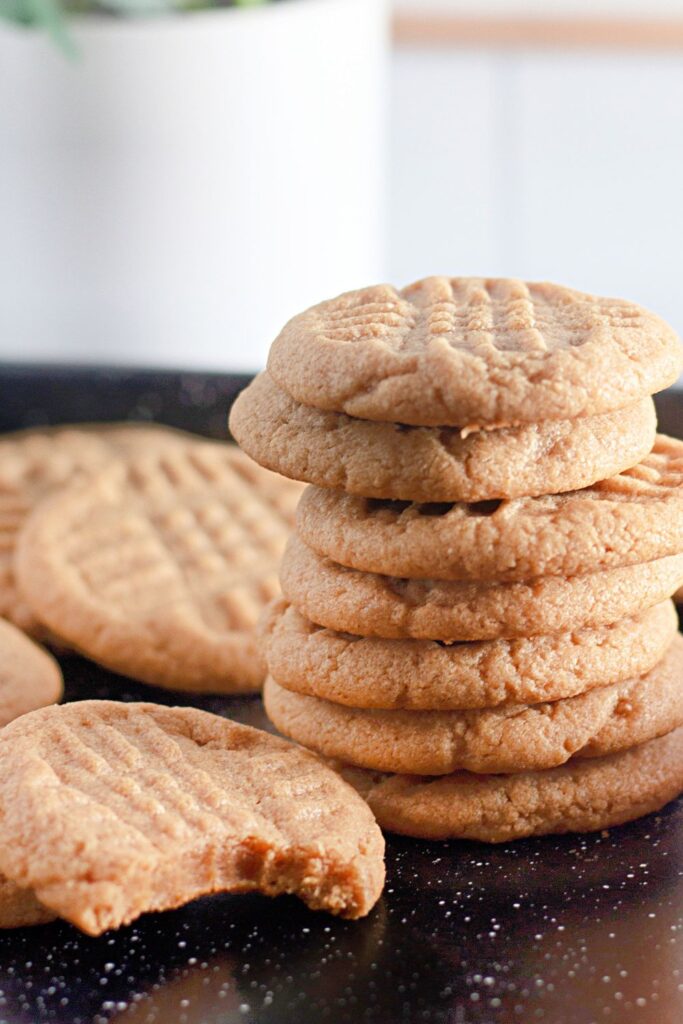 peanut butter cookies on a tray stacked on top of each other and one cookie sat on table with a bite taken out of it