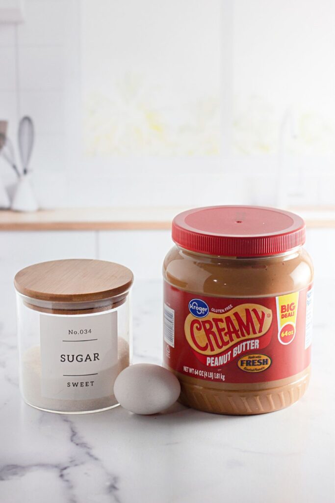jar of granulated sugar, one egg and tub of peanut butter sitting on marble counter