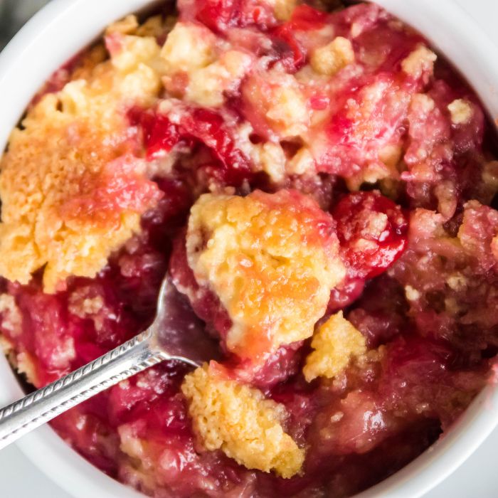 white bowl with cherry pineapple dump cake in it with a spoon on the side