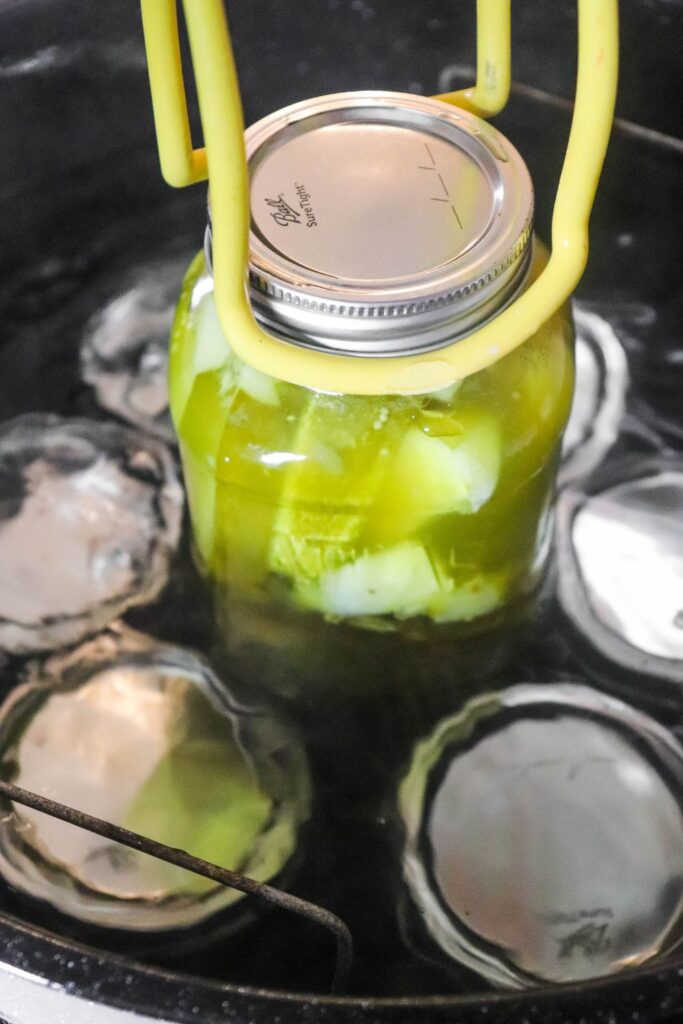 canning jar with pickles going into water bath with tongs