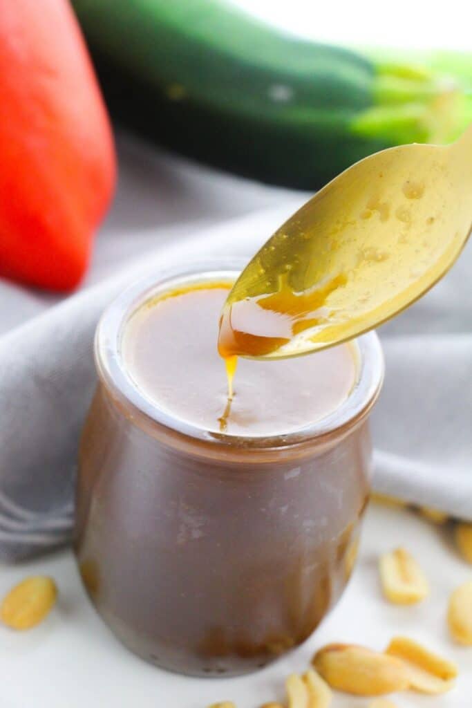 spoon lifting up some kung pao sauce in a jar
