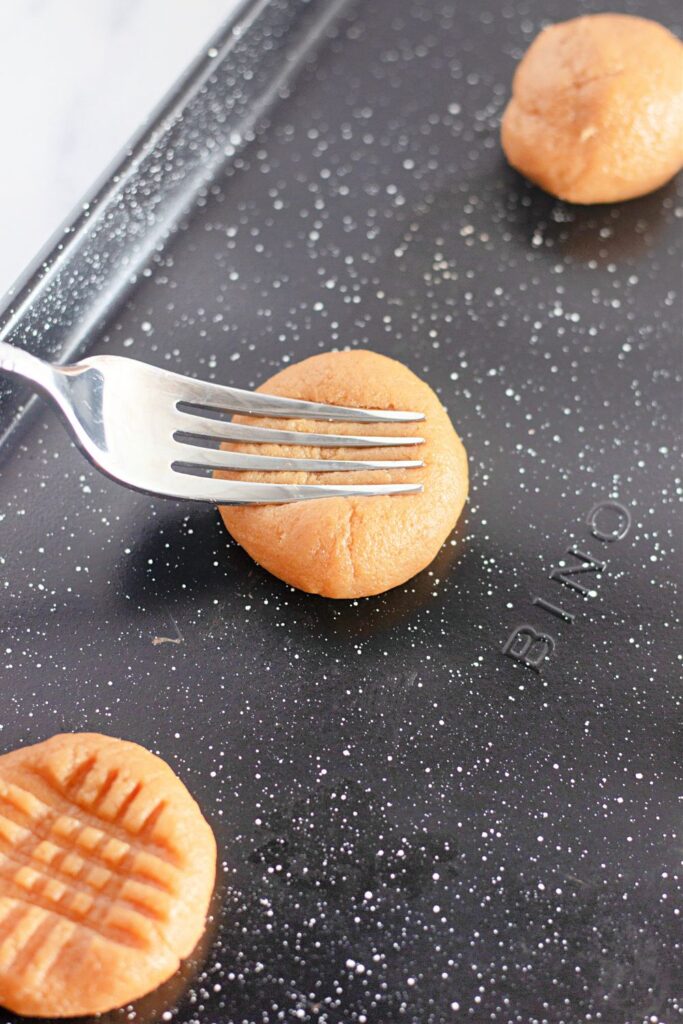 fork pressing into raw peanut butter cookie dough to make the criss-cross pattern