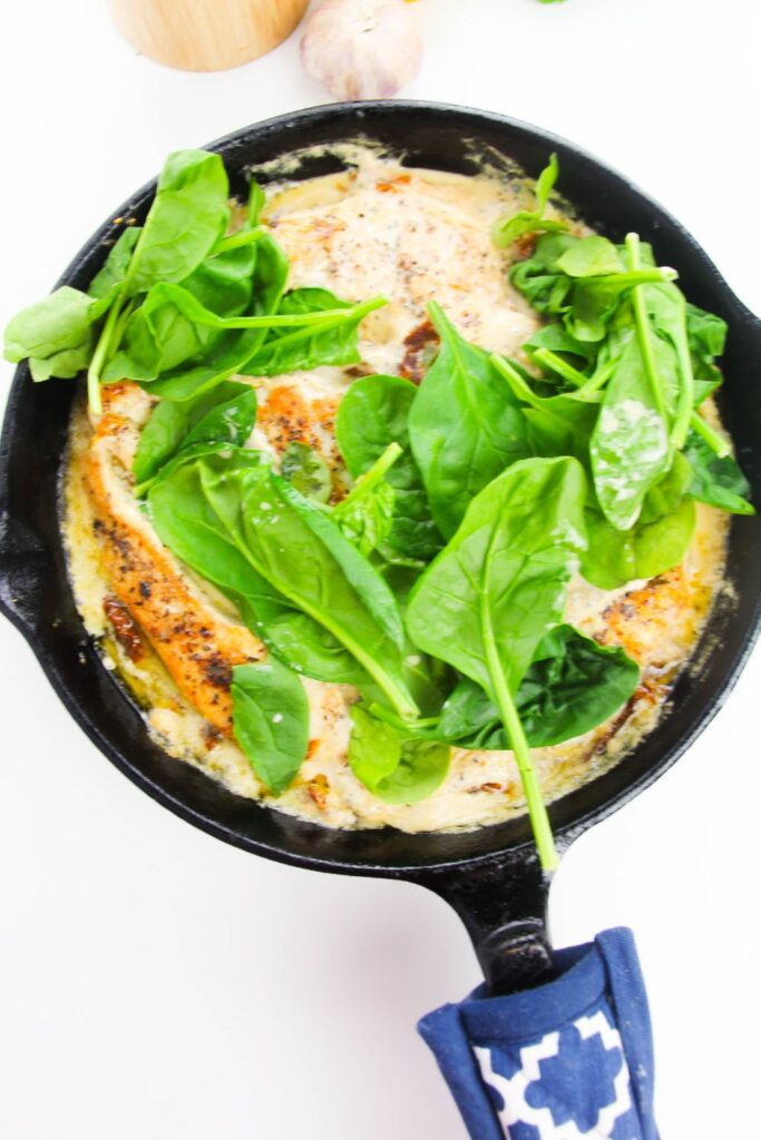 fresh spinach on top of chicken and broth in a cast iron skillet