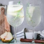 two glasses of white sangria on table with pear on the side